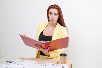 Wall Mural - A red haired girl in a yellow suit sits at a table looking through documents in a red folder