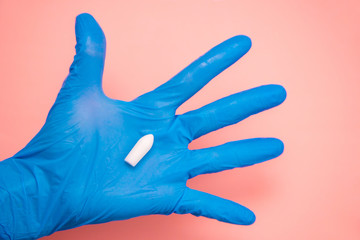 White suppository for anal or vaginal use in hand of a doctor wearing gloves on a pink background. Medical candles for treatment of Candida, thrush, hemorrhoids, inflammation and fever. Copy space