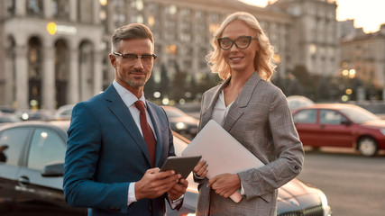 Creating a successful business partnership. Two cheerful colleagues in stylish classic wear looking at camera and smiling while standing outdoors