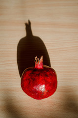 Ripe red fruit pomegranate on a light wooden table under the direct rays of the sun and a hard long shadow, top vertically view