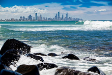 Panoramic View Of Gold Coast Skyscrapers And Buildings From Burleigh Heads Beach, A View From The Sea With Surfers Riding Waves