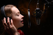 © Anton - A vocalist sings into a studio microphone with headphones on her head, live performance, vocals, vocal studio, recording a track. Against the background of orange smoke