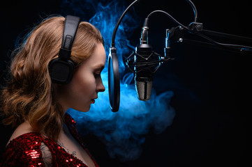 A girl singer sings into a microphone, with a spectacular background, vocals, a recording studio, recording a track. On a black background, with a blue backlight. Vocal school, and training