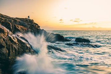 Hiking person on top of a rocky hill near the sea with sea waves crashing