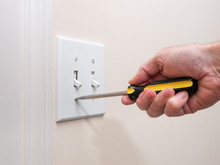 Male Electrician Repairing Wall Light Switch Panel. Handyman Using Screwdriver To Install Screw On Light Switch Cover Plate.