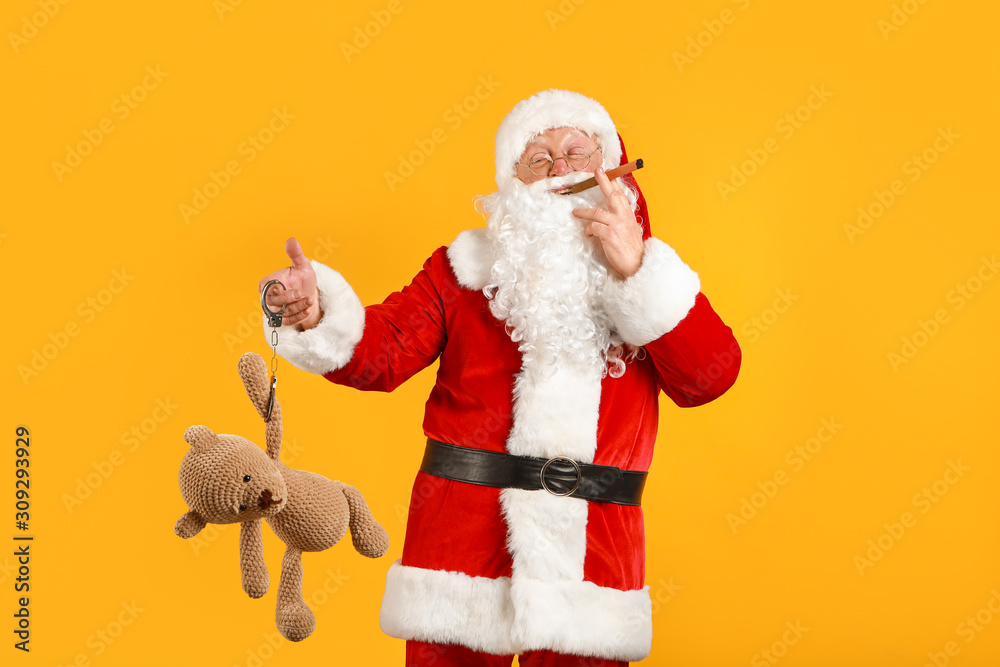 Funny drunk Santa Claus with handcuffs, toy bear and cigar on color background