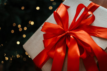 Big Christmas gift box with big red bow. Out of focus Christmas tree in background.