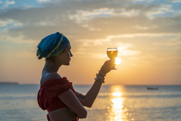 Woman hand holding glass of wine against a beautiful sunset near sea on the tropical beach, close up