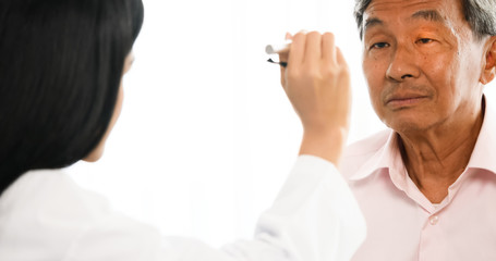 Female doctor checking male patient's eyes at hospital room.