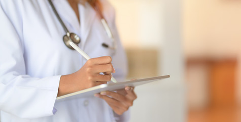 Cropped shot fo young female doctor working on medical records and exam results with tablet in hospital