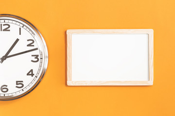 Part of analogue plain wall clock with white board on trendy saffron orange background. One o'clock. Close up banner with copy space, time management or school concept and lunch time