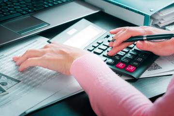 Female accountant in office draws up annual report using income table and calculator. Profit analysis, calculation of taxes, expenses and payments, saving money and budget concept