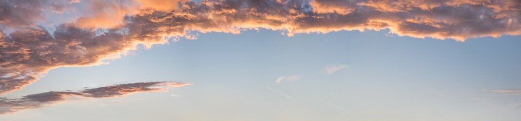 Wall Mural - wide sunset panorama with lighted clouds and blue sky in the lower half