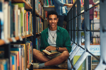 Wall Mural - Young male student study in the library reading book while sitting near bookshelf.