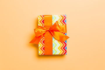 wrapped Christmas or other holiday handmade present in paper with orange ribbon on orange background. Present box, decoration of gift on colored table, top view with copy space