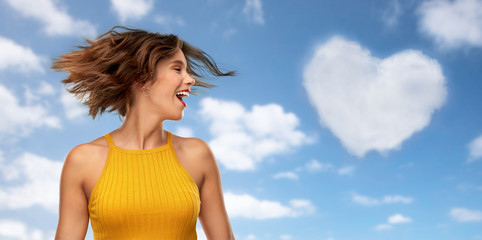 Sticker - emotions and people concept - happy laughing young woman in mustard yellow top shaking head over blue sky and clouds background