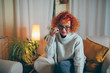 © cherryandbees - red head curly woman sitting sofa at her home using mobile phone