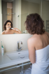 Wall Mural - Pretty, middle aged woman brushing her teeth in a modern design bathroom