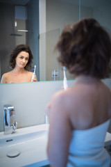 Wall Mural - Pretty, middle aged woman brushing her teeth in a modern design bathroom