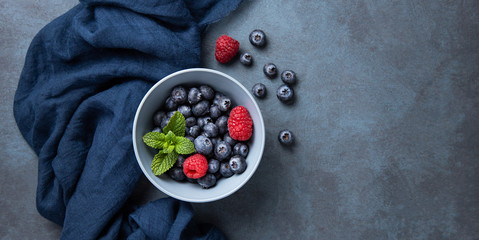 Fresh and sweet blueberry and raspberry in bowl with classic blue napkin  on dark blue wood background