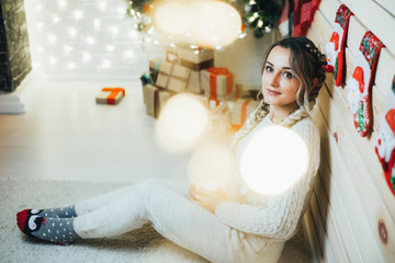 Beautiful young girl with two braids on background of Christmas tree and fireplace