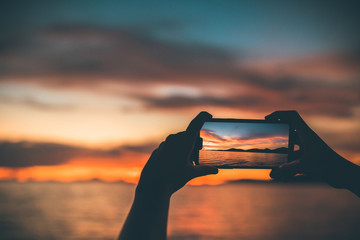 silhouette people use mobile phone take a seascape with sunset.