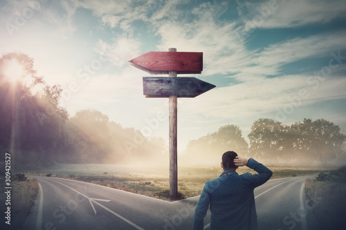 Fotomural Rear businessman in front of crossroad and signpost arrows shows two different courses, left and right direction to choose