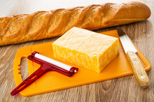 Loaf Of Bread, Piece Of Marble Cheese, Cheese Cutter, Knife On Cutting Board On Wooden Table