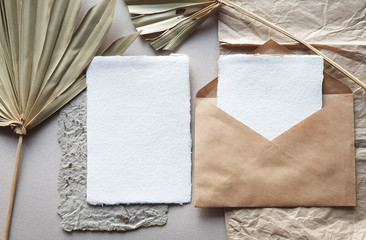 Wall Mural - Blank white Wedding invitation cards mockups with dried palm leaf and craft envelope on textured table backgound. Elegant modern template for branding identity. Tropical design. Flat lay, top view