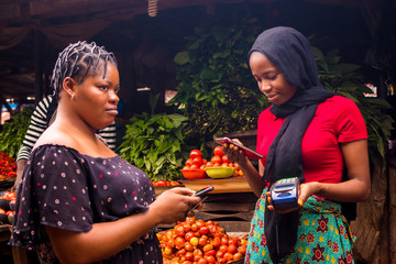 african woman shopping food stuff in a local market paying by doing mobile transfer via phone for a 