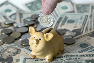 Piggy bank with two euro coin in hand and American dollar usd banknotes on the background