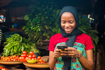 Poster - young african woman selling in a local market smiling while using her mobile phone