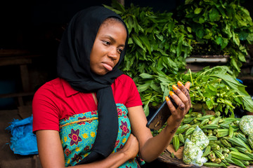 Wall Mural - young african woman selling in a local market feeling sad and dejected while looking at her phone