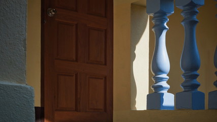 Wall Mural - Sunlight and shadow on surface of vintage blue stone balusters with blurred wooden door in yellow cement wall background, home exterior decoration design concept 