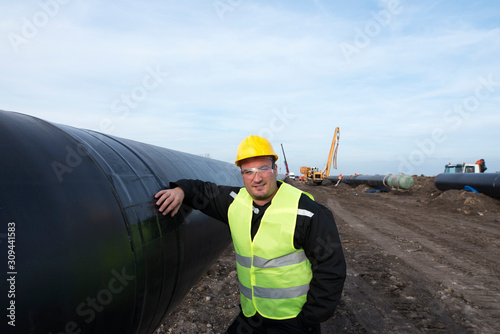 Portrait of an oilfield worker standing by gas pipe at construction site.
