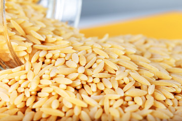 Barley noodles in a jar on yellow wooden background.