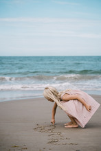 Blond Girl Writing Her Name In The Sand On A Beach