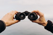 © Isaiah & Taylor Photography/Stocksy - Details of hands holding binoculars looking out toward ocean