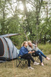 © Maskot - Full length of woman talking to daughter while sitting at campsite