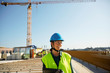 © Maskot - Smiling female engineer in reflective clothing with digital tablet at construction site against clear sky
