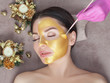 © Dimid - Beautician makes a golden mask to rejuvenate the skin to beautiful woman. Next to her are Christmas decorations.New Year's and Cosmetology concept.