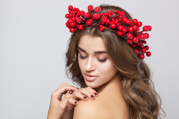 Portrait of a beautiful happy woman  with beautiful hair and nude make-up.She has a wreath of red berries on her head. New Year's concept. Cosmetology skin care and make-up.