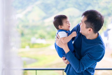 Wall Mural - Attractive young asian father is holding and playing together with his little baby boy at the balcony in the morning time, concept of love, relation and trust and happy moment in family lifestyle .