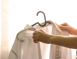 The young man's hands remove the white shirt from the hanger