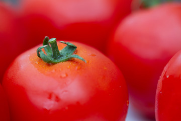 Wall Mural - Details of a red tomato with green stipe and other blurry tomatoes in the background