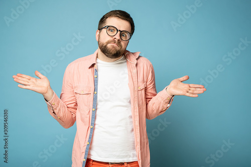 Fotomural Bearded man with an innocent look shrugs, spreads arms to the sides and looks into the camera