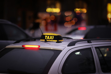 Taxi car with yellow checkered sign on city street in evening, closeup