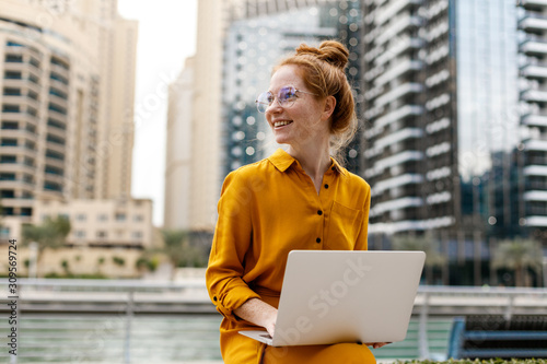 Fotomural Young Woman sitting in Dubai Marina aria and work on laptop