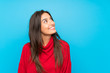 © luismolinero - Young woman with red sweater over isolated blue background laughing and looking up
