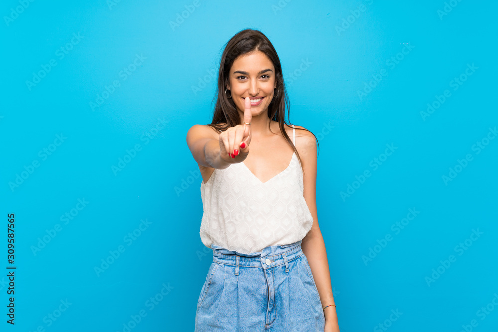 Young woman over isolated blue background showing and lifting a finger - obrazy, fototapety, plakaty 